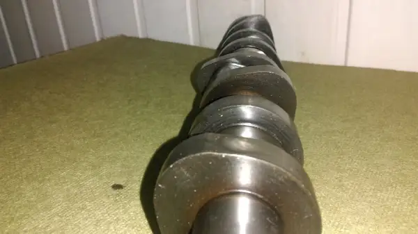 Metalowy wałek rozrządu z widocznymi śladami zużycia, noszący znamiona zatarty wałek rozrządu. Leży na zielonym materiale.