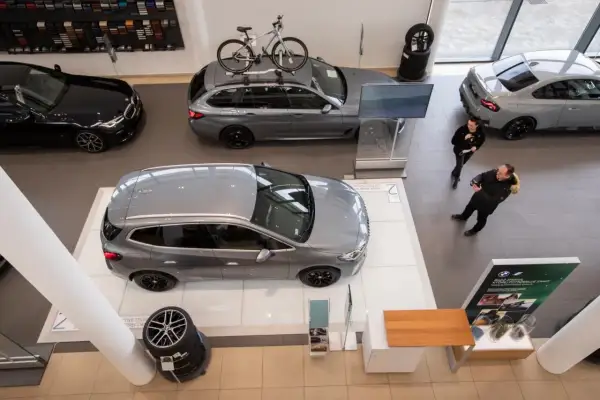 Wnętrze salonu samochodowego, gdzie prezentowane są nowe modele aut. Na pierwszym planie szare kombi, obok czarne BMW. W tle szare coupe i kolejne kombi z rowerem na dachu. Rynek samochodowy w pełnej krasie.