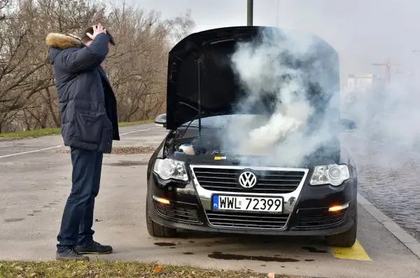 Mężczyzna z przerażeniem patrzy na dym spod maski i czuje zapach spalenizny. Awaria Volkswagena na drodze.