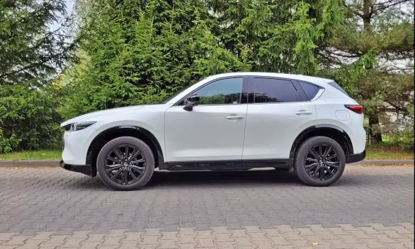 Biała Mazda CX-5 na tle zieleni. Zastanawiasz się nad jej spalaniem? Ten SUV oferuje świetny kompromis między osiągami a ekonomią.