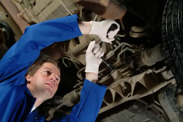 Mechanik w białych rękawiczkach dokręca śrubę pod samochodem. Może to być związane z objawami wybitych tulei tylnej belki.