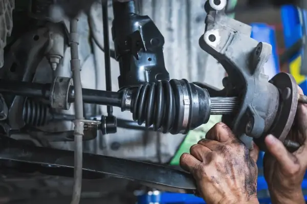 Mechanik wymienia przegub w aucie. Widoczny jest wałek napędowy z gumową osłoną i elementem mocującym.
