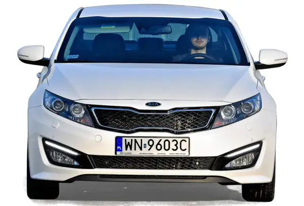 Białe auto z Korei Południowej, model Kia, z młodym kierowcą za kierownicą.