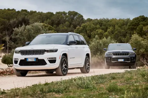 Dwa Jeepy, biały i czarny, jadące po piaszczystej drodze. Jeep kraj pochodzenia to USA, ale te modele wyglądają na europejskie.