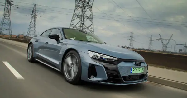 Szary, sportowy Audi GT jedzie po drodze, a w tle widać linie energetyczne i słupy.