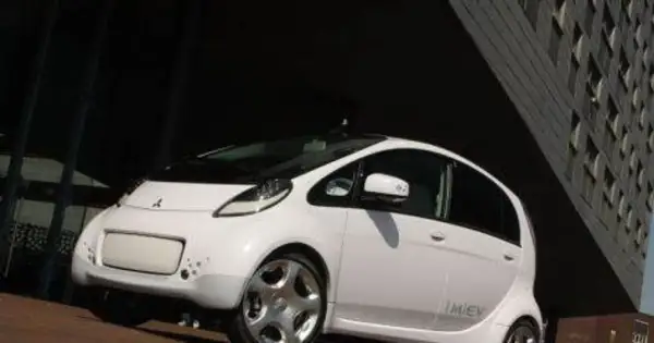Biały, kompaktowy Mitsubishi i-MiEV stoi przed nowoczesnym budynkiem.