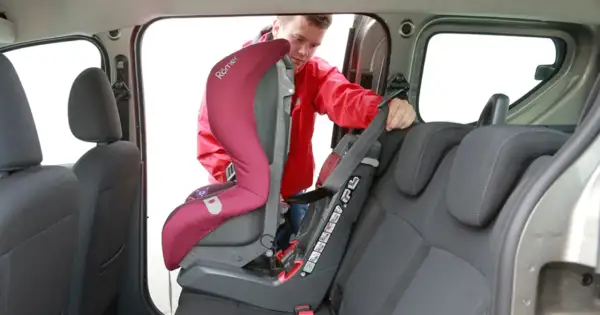 Mężczyzna montuje fotelik dziecięcy. Sprawdź, jak sprawdzić, czy samochód ma isofix, patrząc na zaczepy fotelika.