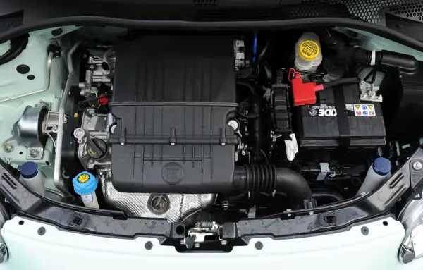 Silniki Fiata 500 w komorze silnika. Widoczny czarny plastikowy element z logo FIAT, akumulator i płyny eksploatacyjne.