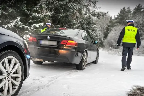 Policjant w kamizelce odblaskowej idzie w stronę czarnego BMW na zaśnieżonej drodze. Kierowca pewnie dostanie mandat za driftowanie.