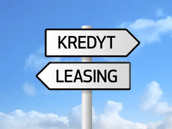 Znak drogowy z napisami "KREDYT" i "LEASING" pod niebieskim niebem z chmurami. Wybór między finansowaniem a zdolnością kredytową.